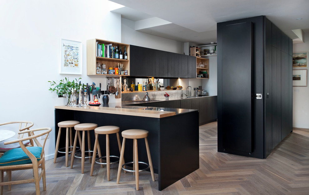 Inredning av ett modernt mellanstort kök, med en integrerad diskho, släta luckor, bänkskiva i rostfritt stål, stänkskydd med metallisk yta, mellanmörkt trägolv, en halv köksö och svarta skåp