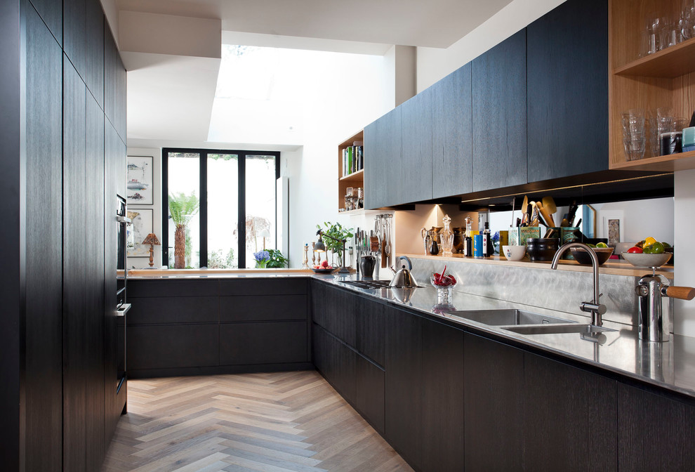 Design ideas for a medium sized contemporary l-shaped kitchen in Dublin with an integrated sink, flat-panel cabinets, stainless steel worktops, metallic splashback, medium hardwood flooring, a breakfast bar and black cabinets.
