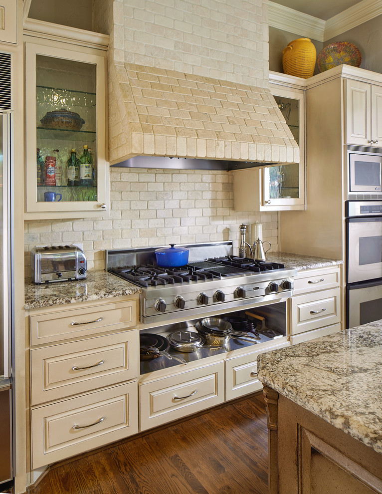 Immagine di una cucina chic con ante con bugna sagomata, ante beige, paraspruzzi beige, paraspruzzi con piastrelle in pietra e elettrodomestici in acciaio inossidabile