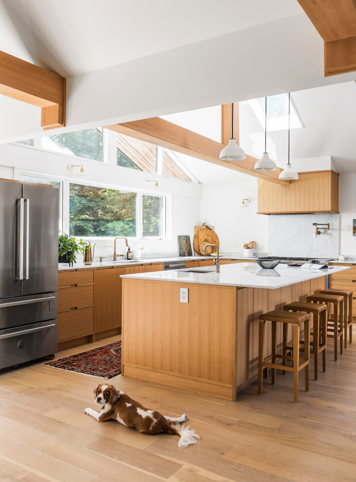 Cette image montre une cuisine design en L et bois brun avec un évier encastré, un placard à porte plane, un électroménager en acier inoxydable, un sol en bois brun, îlot, un sol marron, un plan de travail blanc et un plafond voûté.