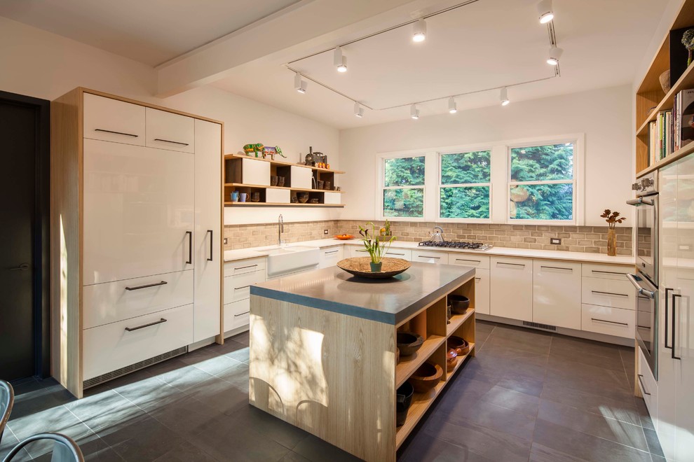 Modern inredning av ett vit vitt kök, med en integrerad diskho, släta luckor, vita skåp, bänkskiva i betong, beige stänkskydd, stänkskydd i mosaik, vita vitvaror, en köksö, svart golv och skiffergolv