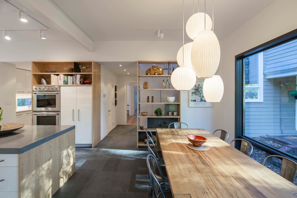Minimalist u-shaped slate floor and black floor eat-in kitchen photo in Boston with flat-panel cabinets, white cabinets, concrete countertops, beige backsplash, an island, gray countertops, a farmhouse sink and paneled appliances
