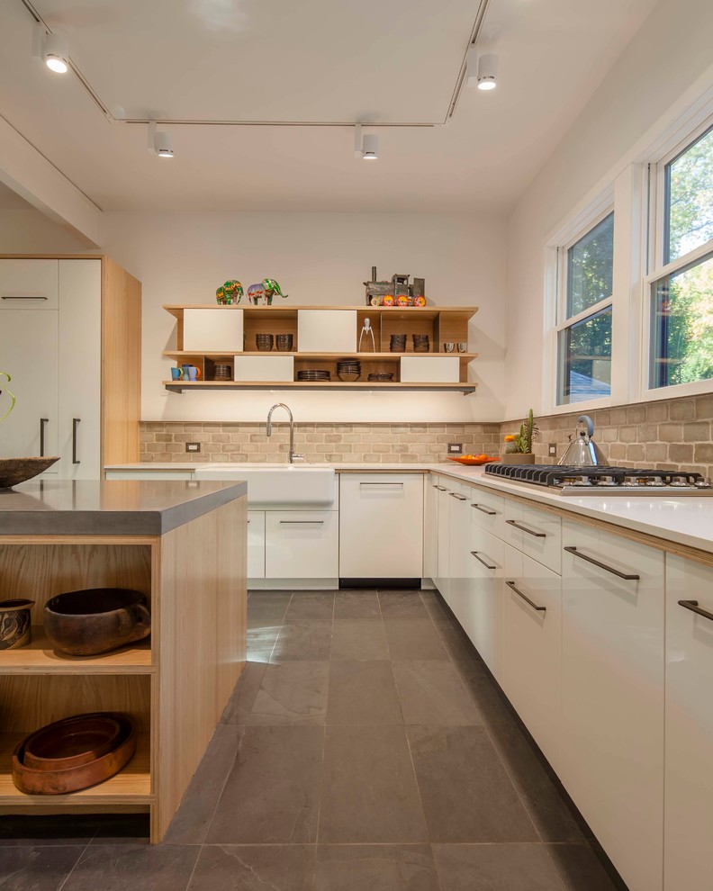 This is an example of a contemporary l-shaped kitchen/diner in Boston with a belfast sink, flat-panel cabinets, white cabinets, grey splashback, integrated appliances, concrete worktops, an island and white worktops.