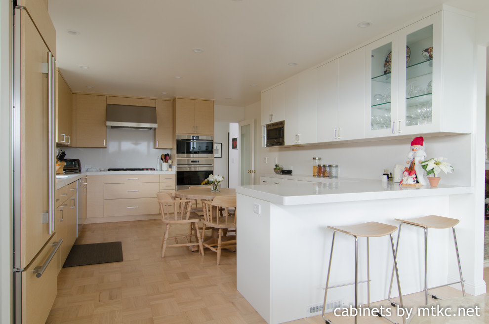 Photo of a medium sized modern l-shaped kitchen/diner in San Francisco with a submerged sink, flat-panel cabinets, light wood cabinets, engineered stone countertops, white splashback, engineered quartz splashback, integrated appliances, light hardwood flooring, a breakfast bar, yellow floors and white worktops.