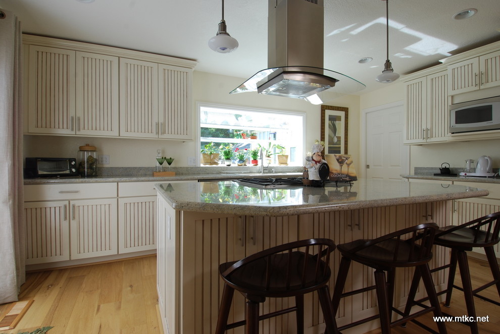 Bild på ett lantligt kök, med en undermonterad diskho, luckor med infälld panel, vita skåp, granitbänkskiva, flerfärgad stänkskydd, stänkskydd i sten, rostfria vitvaror, ljust trägolv, en köksö och gult golv