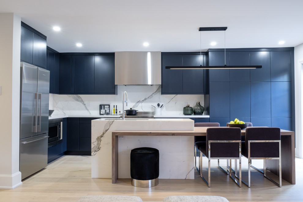 Design ideas for a contemporary l-shaped kitchen/diner in Toronto with flat-panel cabinets, blue cabinets, white splashback, stainless steel appliances, light hardwood flooring, an island, beige floors and white worktops.