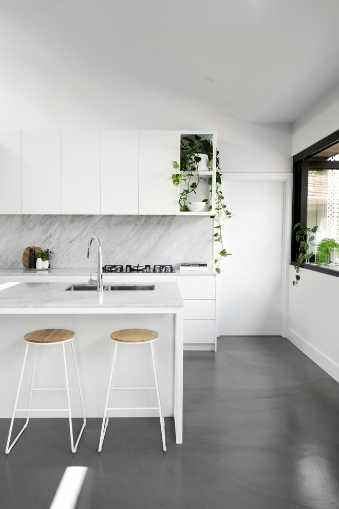 Zweizeilige Moderne Küche mit Unterbauwaschbecken, flächenbündigen Schrankfronten, weißen Schränken, Küchenrückwand in Grau, Betonboden, Kücheninsel, grauem Boden und weißer Arbeitsplatte in Sonstige