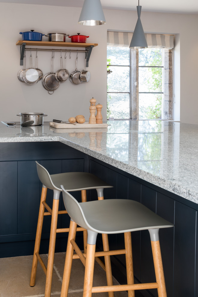 This is an example of a kitchen/diner in Wiltshire with a belfast sink, shaker cabinets, blue cabinets, granite worktops, stainless steel appliances, limestone flooring, an island, beige floors and grey worktops.
