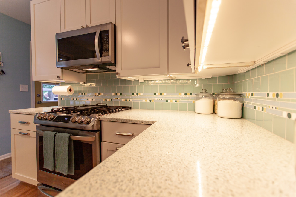 Retro inredning av ett avskilt vit vitt kök, med en undermonterad diskho, skåp i shakerstil, vita skåp, bänkskiva i återvunnet glas, grönt stänkskydd, stänkskydd i mosaik, rostfria vitvaror, mellanmörkt trägolv och brunt golv