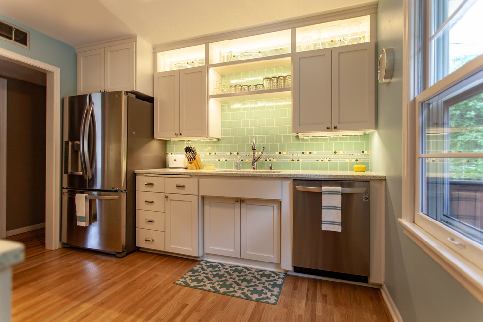 Inspiration for a 1950s medium tone wood floor and brown floor enclosed kitchen remodel in Minneapolis with an undermount sink, shaker cabinets, white cabinets, recycled glass countertops, green backsplash, mosaic tile backsplash, stainless steel appliances, no island and white countertops