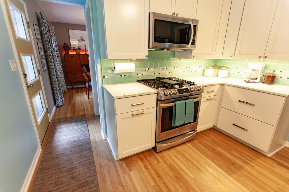 Photo of a retro enclosed kitchen in Minneapolis with a submerged sink, shaker cabinets, white cabinets, recycled glass countertops, green splashback, mosaic tiled splashback, stainless steel appliances, medium hardwood flooring, no island, brown floors and white worktops.