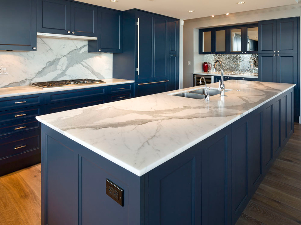 Example of a mid-sized transitional l-shaped medium tone wood floor and brown floor open concept kitchen design in Vancouver with an undermount sink, recessed-panel cabinets, blue cabinets, marble countertops, white backsplash, marble backsplash, stainless steel appliances and an island
