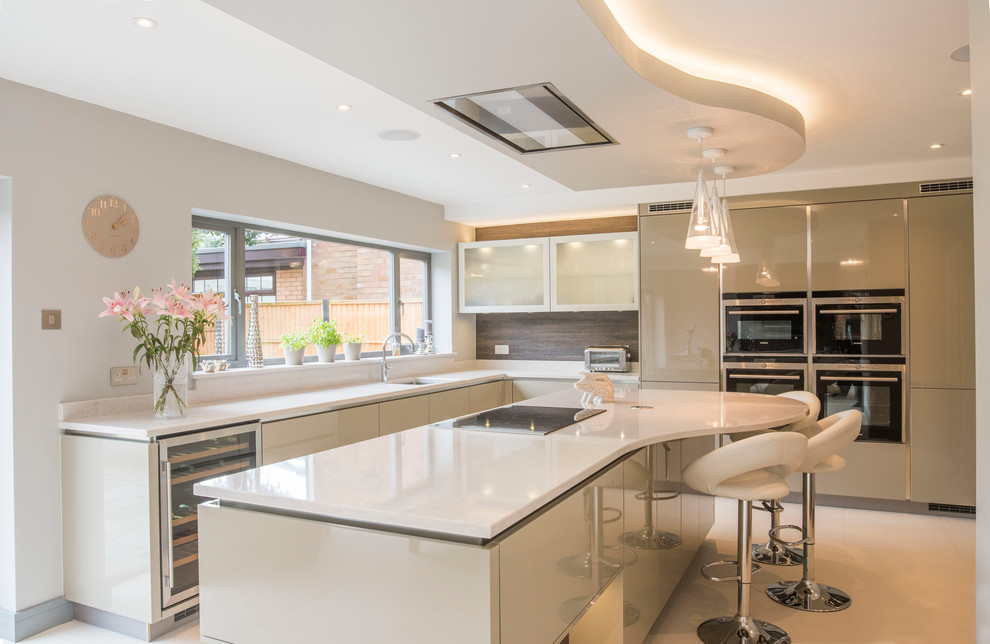 This is an example of a contemporary kitchen in West Midlands with flat-panel cabinets, beige cabinets, brown splashback, an island, white floors and white worktops.
