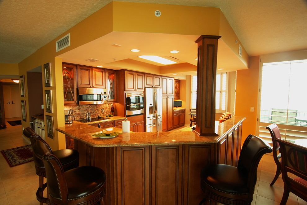 Example of a classic u-shaped ceramic tile kitchen design in Miami with raised-panel cabinets, medium tone wood cabinets, stone tile backsplash, stainless steel appliances and an island