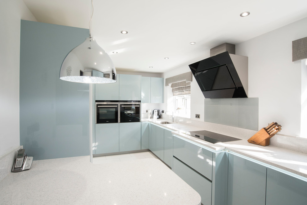 Moderne Küche mit flächenbündigen Schrankfronten, blauen Schränken, Unterbauwaschbecken, Küchenrückwand in Grau, Halbinsel und grauer Arbeitsplatte in West Midlands