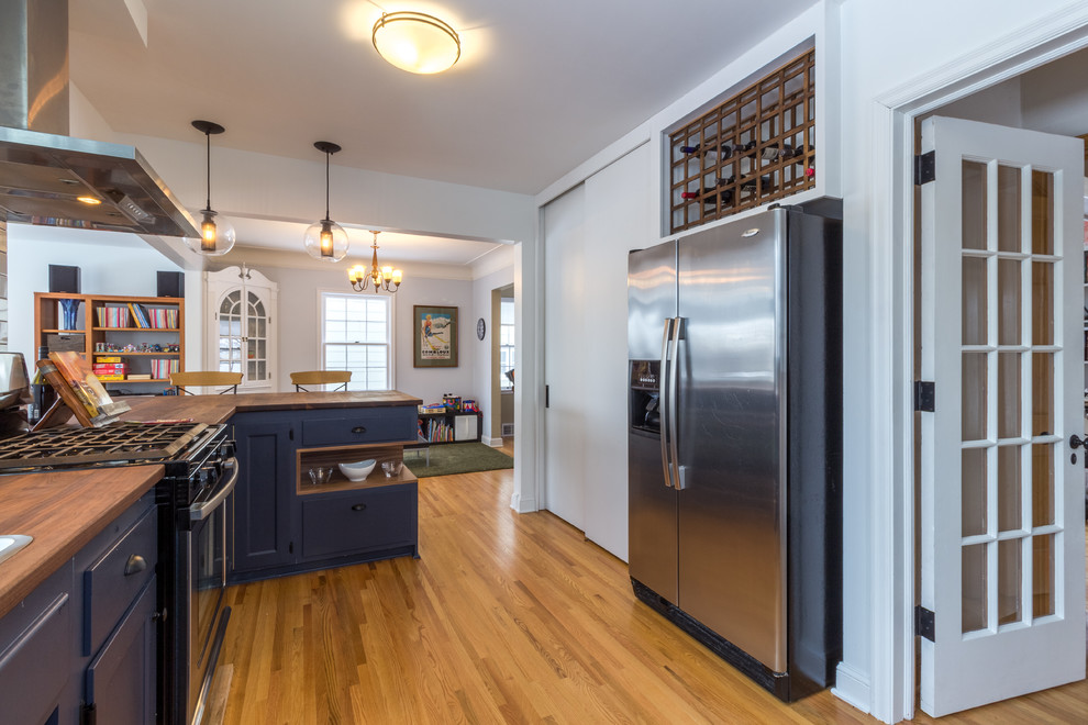 Large danish l-shaped medium tone wood floor and brown floor open concept kitchen photo in Minneapolis with a double-bowl sink, recessed-panel cabinets, blue cabinets, wood countertops, white backsplash, subway tile backsplash, stainless steel appliances and a peninsula