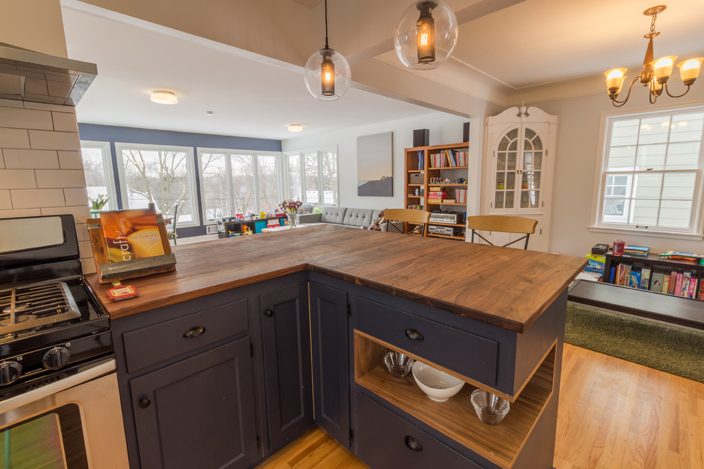 Example of a large danish l-shaped medium tone wood floor and brown floor open concept kitchen design in Minneapolis with a double-bowl sink, recessed-panel cabinets, blue cabinets, wood countertops, white backsplash, subway tile backsplash, stainless steel appliances and a peninsula