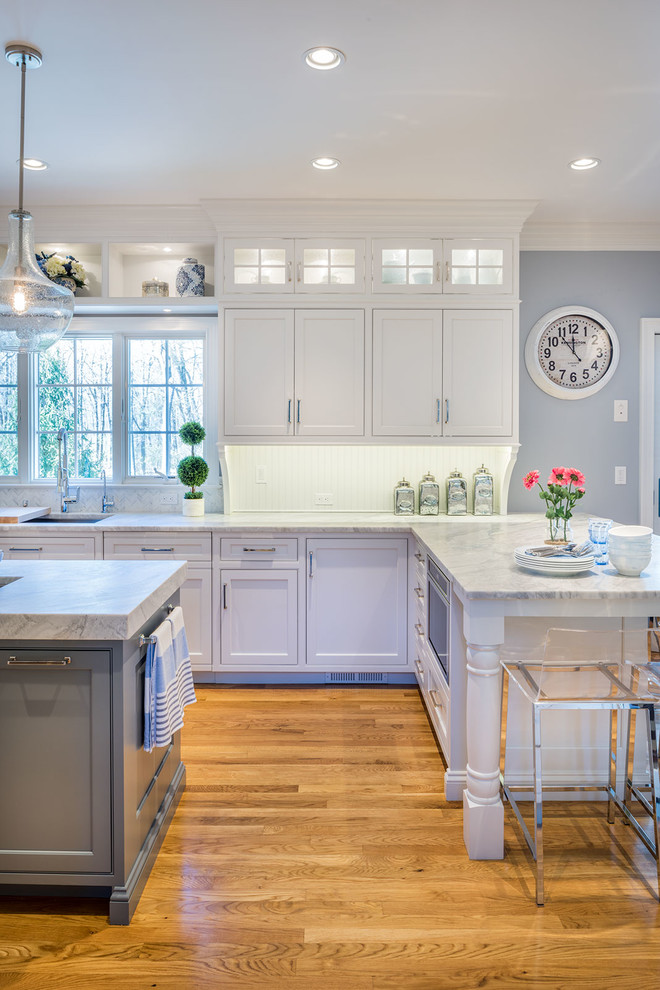 Example of a large transitional u-shaped medium tone wood floor enclosed kitchen design in New York with an undermount sink, beaded inset cabinets, white cabinets, marble countertops, white backsplash, stone tile backsplash, stainless steel appliances and an island