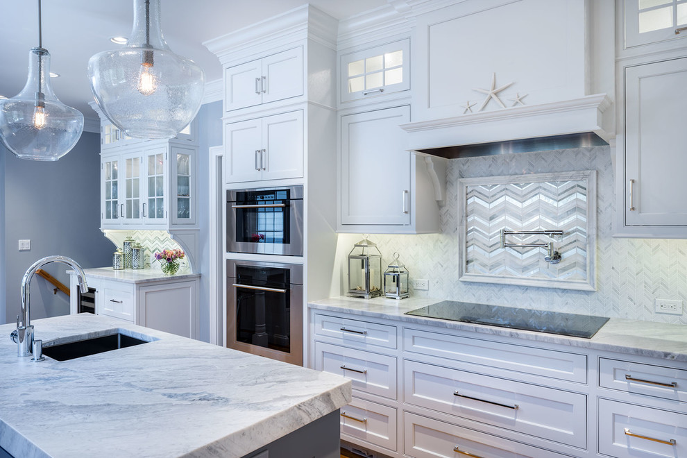 Example of a large transitional u-shaped medium tone wood floor enclosed kitchen design in New York with an undermount sink, beaded inset cabinets, white cabinets, marble countertops, white backsplash, stone tile backsplash, stainless steel appliances and an island