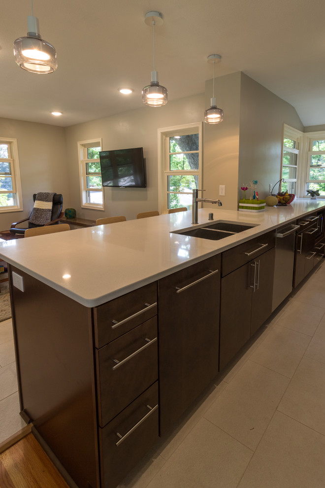 Photo of a midcentury open plan kitchen in Minneapolis with a double-bowl sink, dark wood cabinets, engineered stone countertops, white splashback, stainless steel appliances, ceramic flooring, a breakfast bar and beige floors.