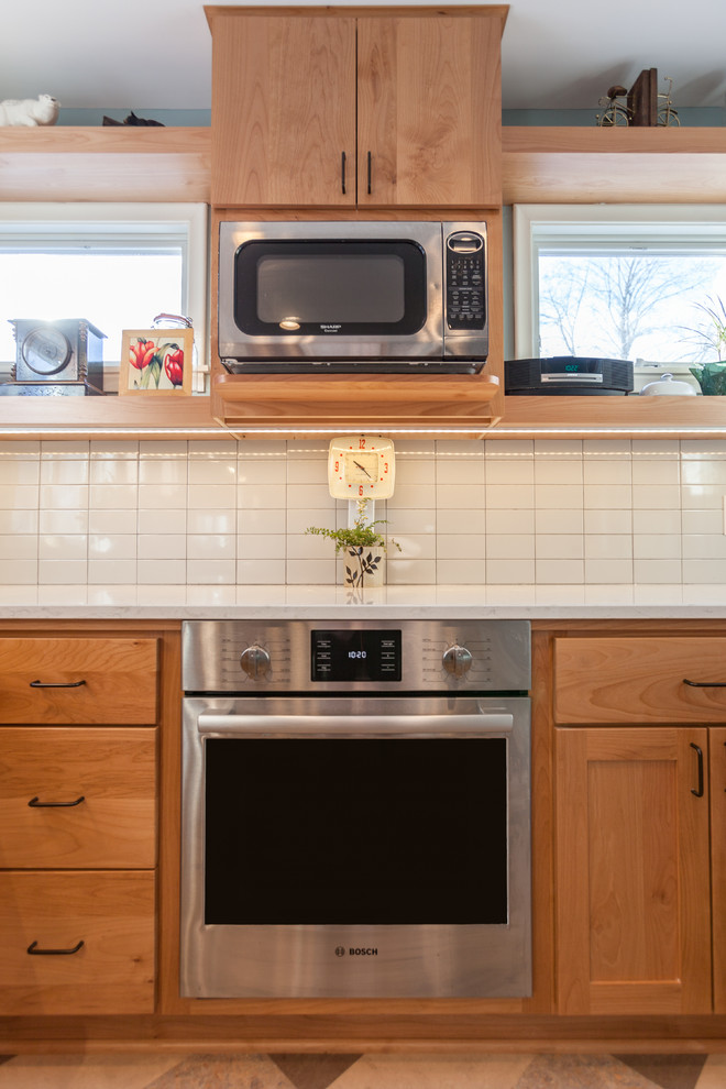 ミネアポリスにある中くらいな北欧スタイルのおしゃれなキッチン (アンダーカウンターシンク、フラットパネル扉のキャビネット、淡色木目調キャビネット、クオーツストーンカウンター、白いキッチンパネル、セラミックタイルのキッチンパネル、シルバーの調理設備、リノリウムの床、マルチカラーの床、白いキッチンカウンター) の写真