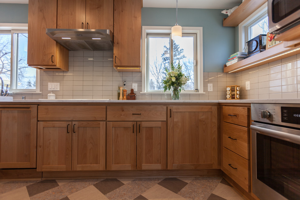 Inspiration for a mid-sized scandinavian u-shaped linoleum floor and multicolored floor enclosed kitchen remodel in Minneapolis with an undermount sink, flat-panel cabinets, light wood cabinets, quartz countertops, white backsplash, ceramic backsplash, stainless steel appliances, an island and white countertops