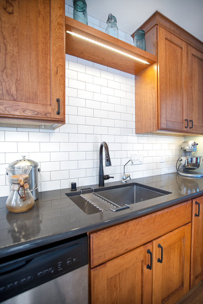 Photo of a medium sized traditional l-shaped kitchen/diner in Minneapolis with a submerged sink, recessed-panel cabinets, medium wood cabinets, engineered stone countertops, white splashback, ceramic splashback, stainless steel appliances, light hardwood flooring, a breakfast bar, brown floors and grey worktops.