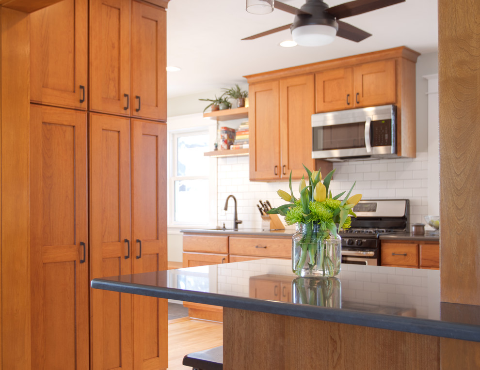 Idéer för att renovera ett mellanstort amerikanskt grå grått kök, med en undermonterad diskho, luckor med infälld panel, skåp i mellenmörkt trä, bänkskiva i kvarts, vitt stänkskydd, stänkskydd i keramik, rostfria vitvaror, ljust trägolv, en halv köksö och brunt golv