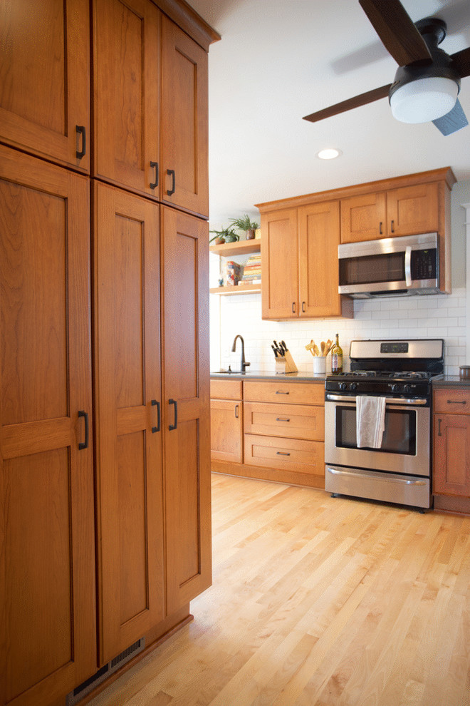 Inspiration för mellanstora amerikanska grått kök, med en undermonterad diskho, luckor med infälld panel, skåp i mellenmörkt trä, bänkskiva i kvarts, vitt stänkskydd, stänkskydd i keramik, rostfria vitvaror, ljust trägolv, en halv köksö och brunt golv