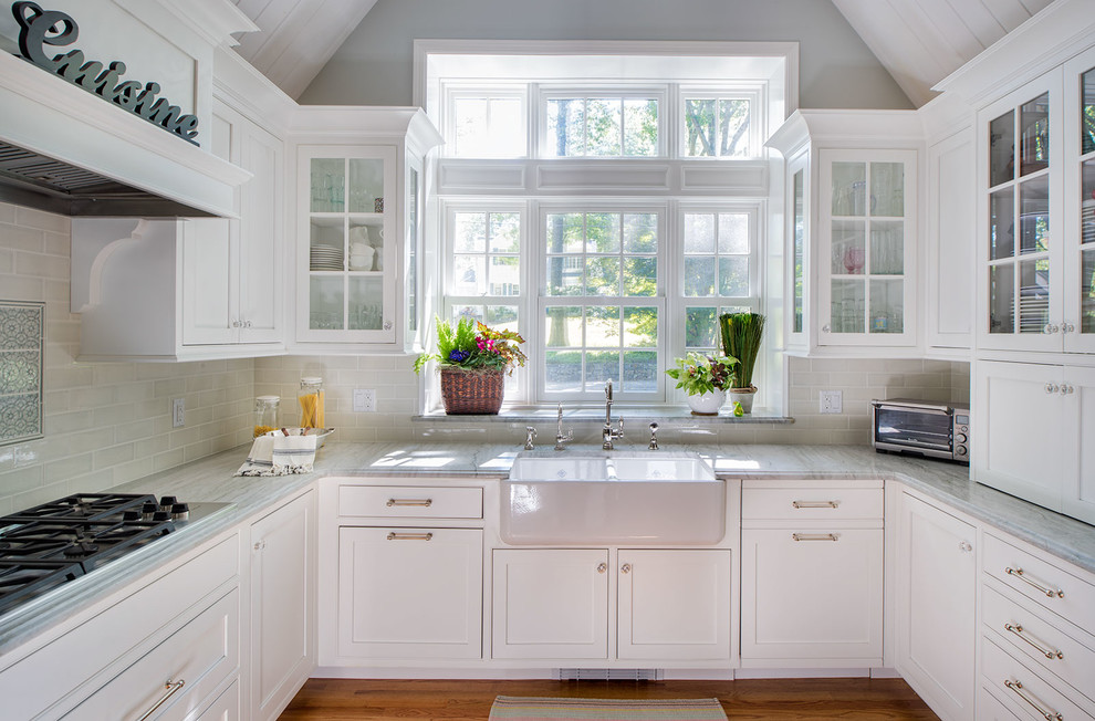 Inspiration for a mid-sized farmhouse u-shaped medium tone wood floor eat-in kitchen remodel in New York with a farmhouse sink, raised-panel cabinets, white cabinets, marble countertops, multicolored backsplash, ceramic backsplash, stainless steel appliances and a peninsula