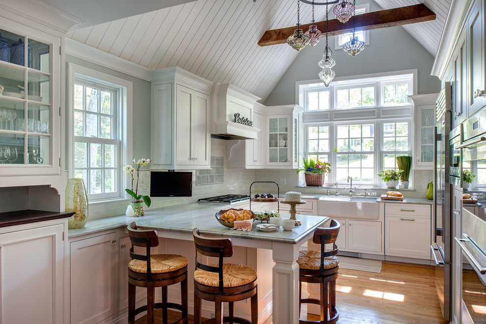 Inspiration for a mid-sized timeless u-shaped medium tone wood floor eat-in kitchen remodel in New York with a farmhouse sink, raised-panel cabinets, white cabinets, marble countertops, multicolored backsplash, ceramic backsplash, stainless steel appliances and a peninsula