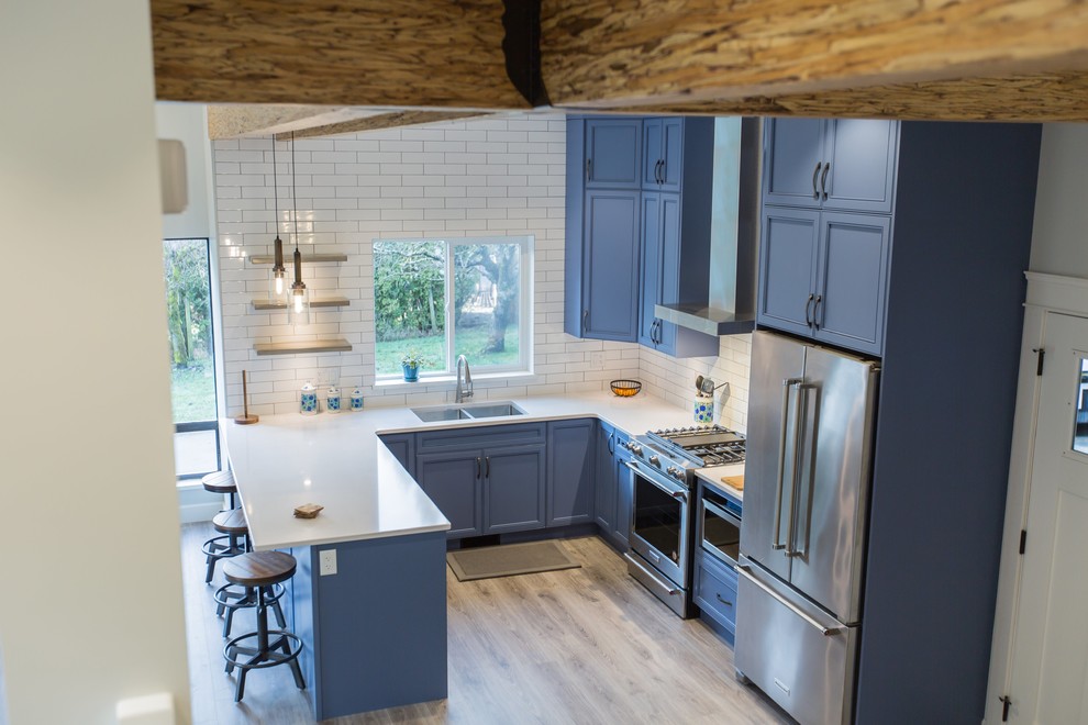 Mid-sized country u-shaped light wood floor and beige floor kitchen photo in Vancouver with an undermount sink, recessed-panel cabinets, blue cabinets, quartzite countertops, white backsplash, subway tile backsplash, stainless steel appliances, a peninsula and white countertops