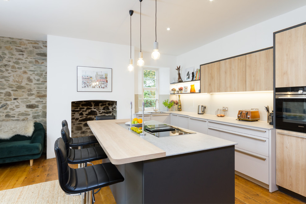 Photo of a medium sized contemporary l-shaped kitchen in Devon with a double-bowl sink, flat-panel cabinets, stainless steel appliances, light hardwood flooring, an island, brown floors and grey worktops.