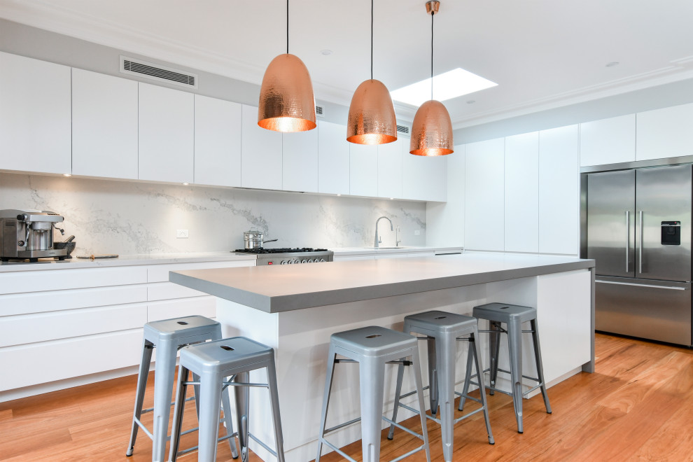 Moderne Küche in L-Form mit flächenbündigen Schrankfronten, weißen Schränken, Küchenrückwand in Grau, Küchengeräten aus Edelstahl, braunem Holzboden, Kücheninsel und braunem Boden in Sydney