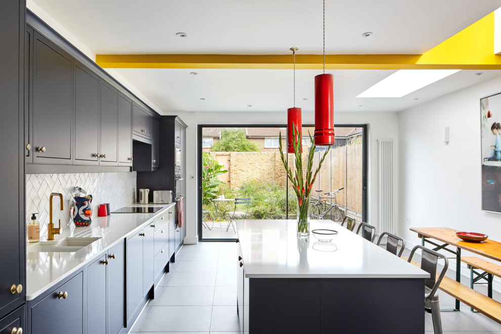 Photo of a medium sized traditional single-wall kitchen/diner in London with an integrated sink, shaker cabinets, blue cabinets, composite countertops, white splashback, porcelain splashback, integrated appliances, porcelain flooring, an island, grey floors, white worktops and exposed beams.