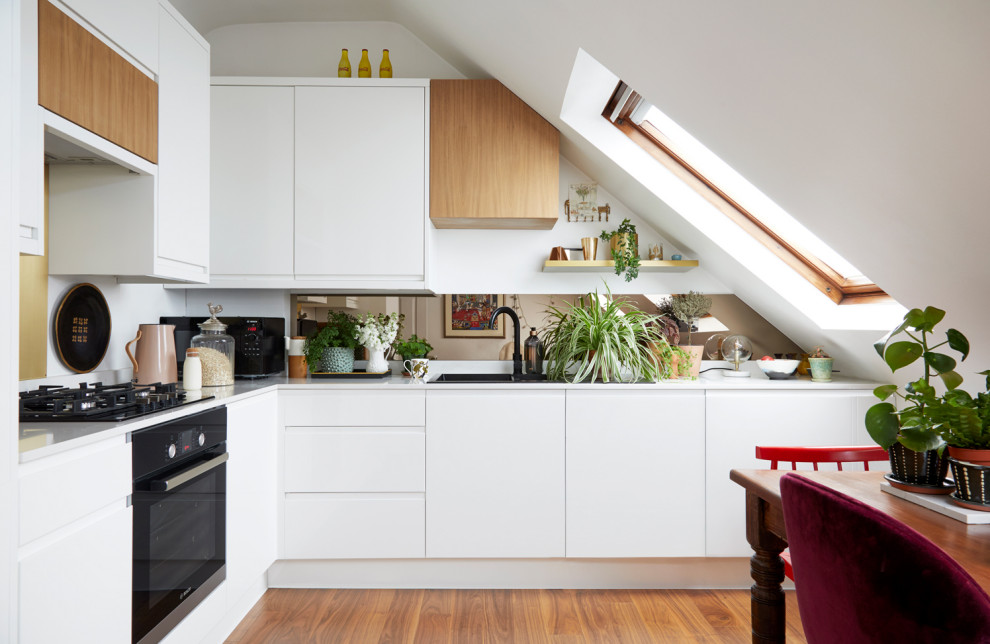 Photo of a contemporary l-shaped kitchen in London with a built-in sink, flat-panel cabinets, white cabinets, mirror splashback, medium hardwood flooring, brown floors and white worktops.