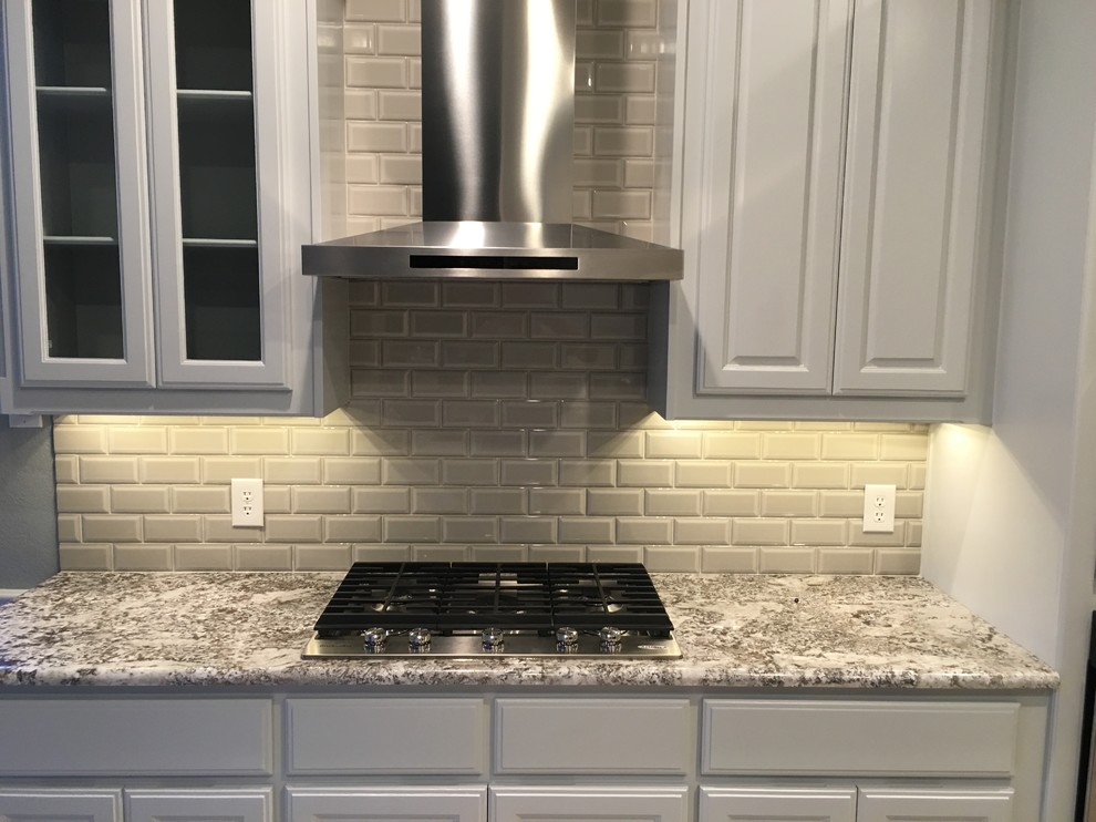 This is an example of a large classic u-shaped enclosed kitchen in Dallas with raised-panel cabinets, white cabinets, granite worktops, grey splashback, metro tiled splashback, stainless steel appliances, a submerged sink, ceramic flooring, an island and beige floors.