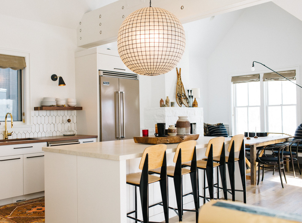 Bild på ett nordiskt kök, med en enkel diskho, släta luckor, vita skåp, träbänkskiva, vitt stänkskydd, en köksö och rostfria vitvaror