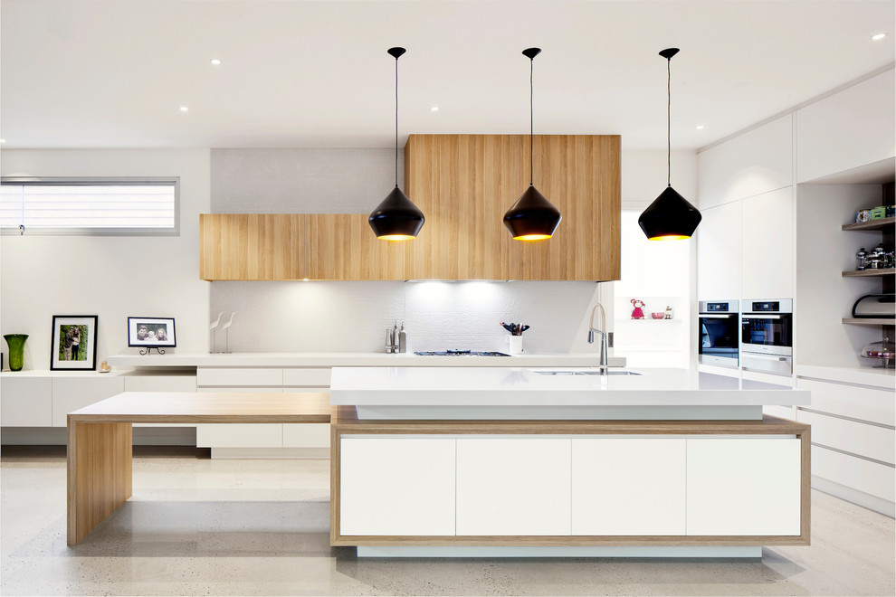 Diseño de cocinas en L contemporánea de tamaño medio con fregadero bajoencimera, armarios con paneles lisos, puertas de armario de madera clara, salpicadero blanco y una isla