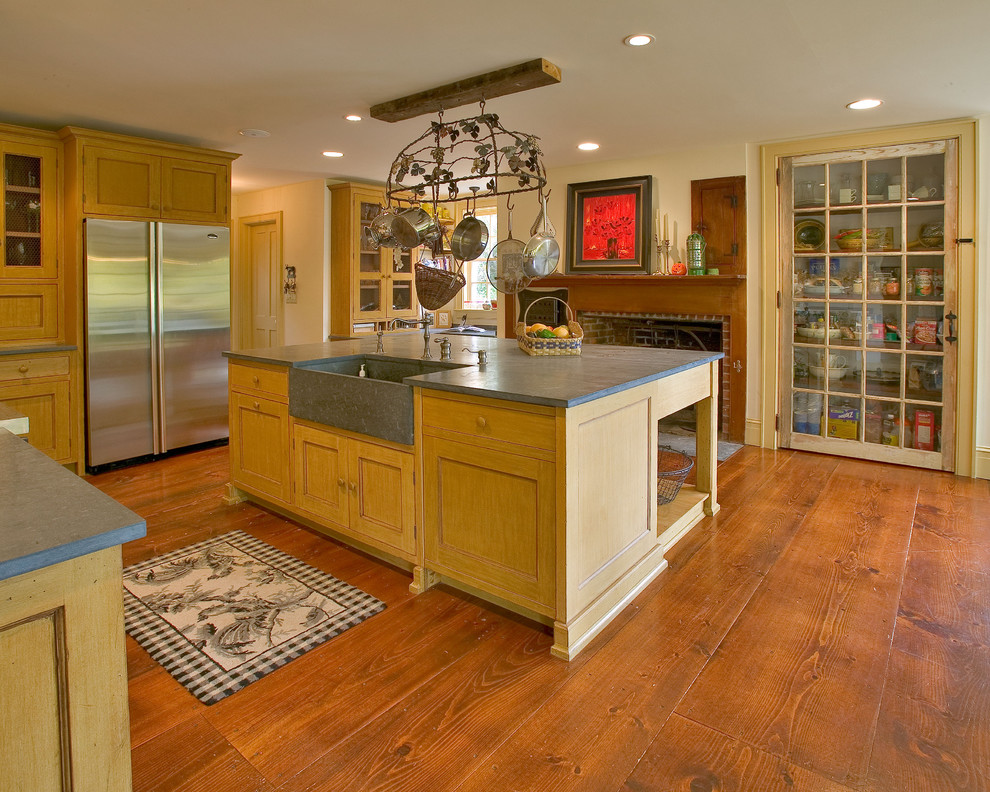 Klassisk inredning av ett stort kök, med en rustik diskho, rostfria vitvaror, luckor med infälld panel, gula skåp, bänkskiva i täljsten, mellanmörkt trägolv och en köksö