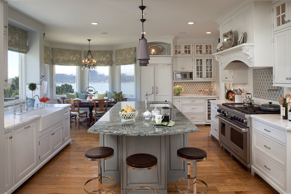 Example of a classic medium tone wood floor kitchen design in San Francisco with a farmhouse sink, shaker cabinets, granite countertops, ceramic backsplash, an island, paneled appliances and white cabinets