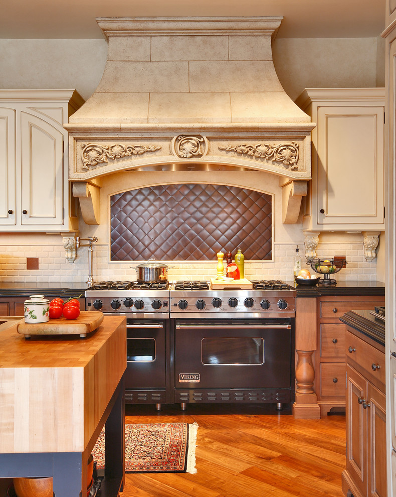Mid-sized elegant medium tone wood floor and brown floor kitchen photo in New York with stainless steel appliances, flat-panel cabinets, medium tone wood cabinets, wood countertops, gray backsplash, subway tile backsplash and an island