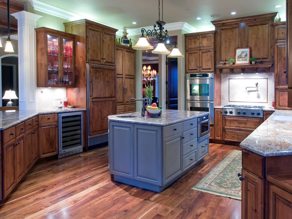 Inspiration for a mid-sized timeless u-shaped medium tone wood floor kitchen remodel in Portland with raised-panel cabinets, dark wood cabinets, white backsplash, stainless steel appliances, solid surface countertops, ceramic backsplash and an island