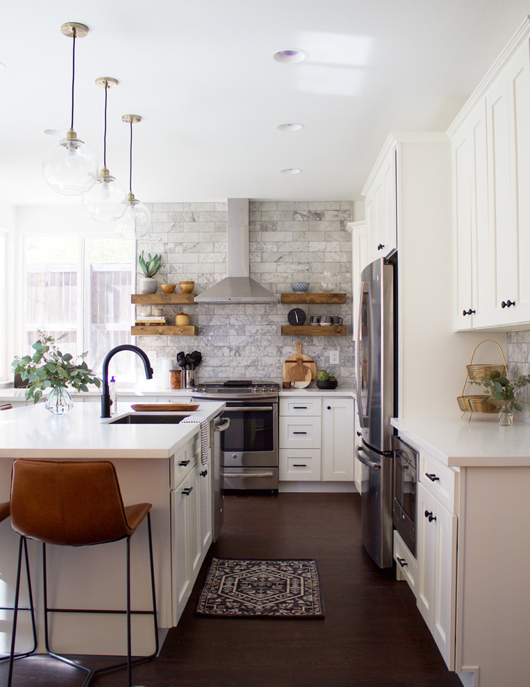 Foto på ett vintage l-kök, med en undermonterad diskho, skåp i shakerstil, vita skåp, bänkskiva i kvarts, grått stänkskydd, stänkskydd i marmor, rostfria vitvaror, laminatgolv, en köksö och brunt golv