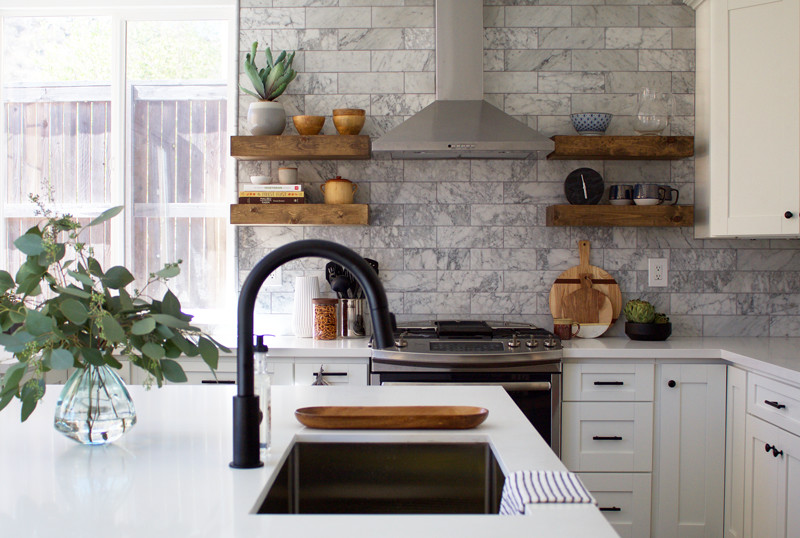 Lantlig inredning av ett kök, med en undermonterad diskho, skåp i shakerstil, vita skåp, bänkskiva i kvarts, grått stänkskydd, stänkskydd i marmor, rostfria vitvaror, laminatgolv, en köksö och brunt golv