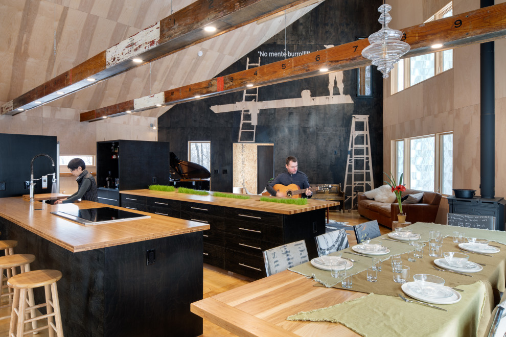 Inredning av ett modernt stort kök och matrum, med en undermonterad diskho, släta luckor, svarta skåp, träbänkskiva, rostfria vitvaror, plywoodgolv och flera köksöar