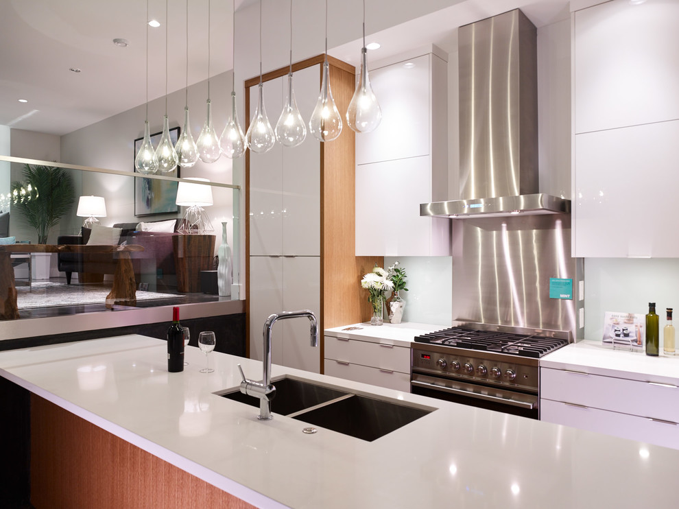 Inredning av ett modernt mellanstort kök, med en undermonterad diskho, släta luckor, vita skåp, bänkskiva i kvarts, vitt stänkskydd, glaspanel som stänkskydd, rostfria vitvaror, betonggolv och en köksö