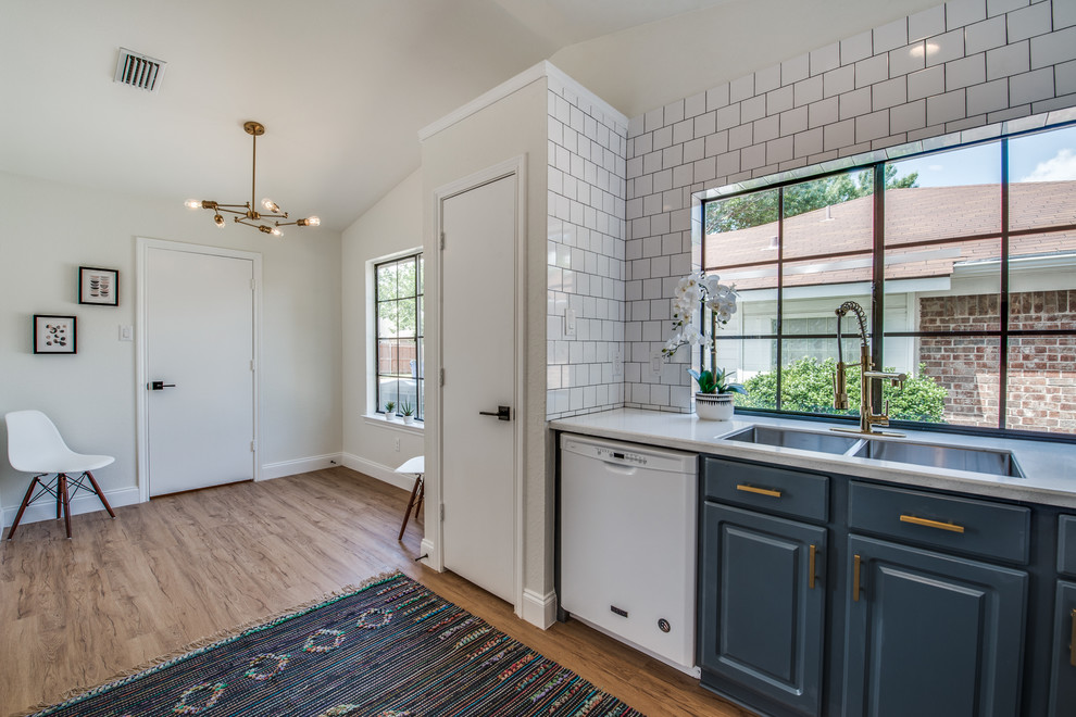 Example of a 1950s u-shaped light wood floor and brown floor eat-in kitchen design in Dallas with an undermount sink, raised-panel cabinets, blue cabinets, quartz countertops, white backsplash, subway tile backsplash, white appliances and white countertops