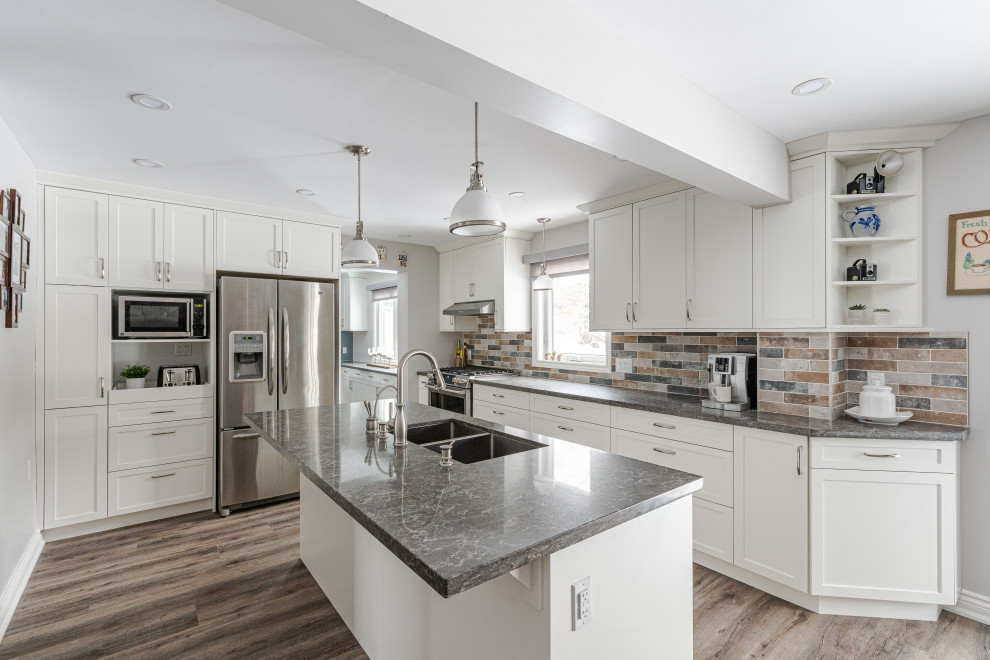 This is an example of a medium sized country l-shaped kitchen in Toronto with a double-bowl sink, shaker cabinets, white cabinets, quartz worktops, multi-coloured splashback, brick splashback, stainless steel appliances, vinyl flooring, an island, brown floors and grey worktops.