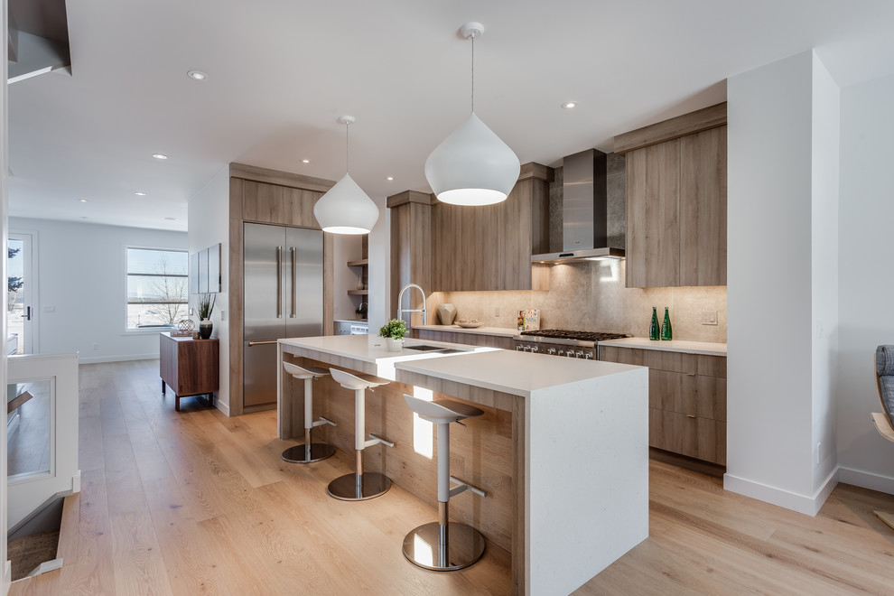Example of a trendy galley light wood floor and beige floor open concept kitchen design in Calgary with flat-panel cabinets, light wood cabinets, beige backsplash, stainless steel appliances and an island
